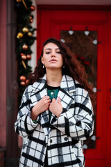 Stylish woman in checkered coat in front of the red door with Christmas festive decorations