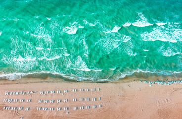 Aerial drone top down shot of empty beach and clean blue sea. Beautiful beach with empty sunbeds. Summer holiday background view.