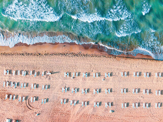 Aerial drone top down shot of empty beach and clean blue sea. Beautiful beach with empty sunbeds. Summer holiday background view.