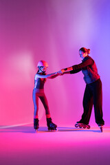 Fototapeta premium child skater athlete holding hands of her trainer, training for competition, photo on pink background in a studio 