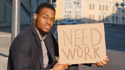 Looking for job. Fired millennial upset male. Businessman loosing business and searching employment in crisis. Sad mixed race young adult black man sitting outdoor with cardboard text table Need Work