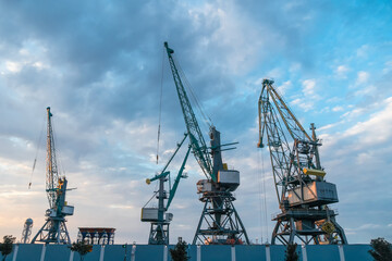 Fototapeta na wymiar Port cranes close-up against a beautiful blue sky with clouds before sunset. Cargo terminal. Batumi, Georgia