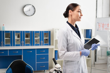 Scientist holding digital tablet with blank screen near microscope in lab.