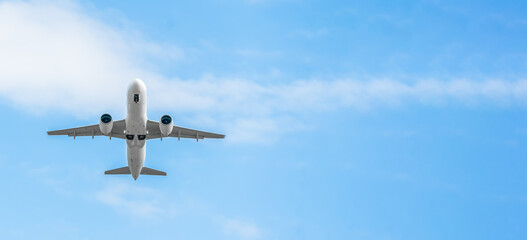 Low-flying white passenger plane with landing gear on a background of blue sky with clouds with copy space, bottom view. Plane took off and hides the landing gear in flight. Banner