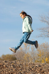 Girl in a jump. A little girl (nine years old) jumps high outdoors in a park. Autumn. Sky is blue. One person