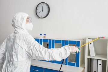 scientist in protective suit making disinfection of lab with sprayer.