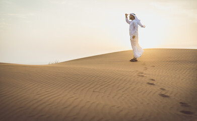 Arabic man with traditional emirates clothes walking in the desert