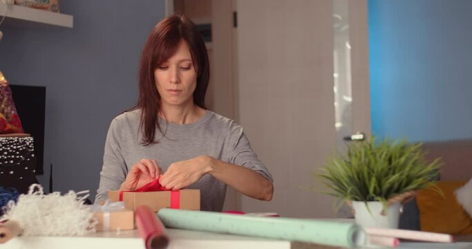Young woman wrapping gift box by festive ribbon at home. Happy holiday present and giftsYoung woman wrapping gift box by festive ribbon at home. Happy holiday present and giftsYoung woman wrapping gif