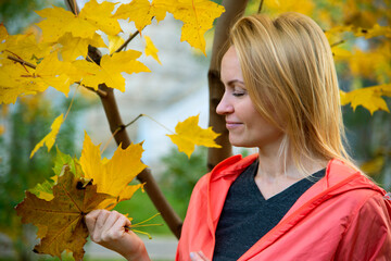 Portrait of a beautiful blonde girl with a smile outdoors in the park against the background of yellow autumn leaves on trees