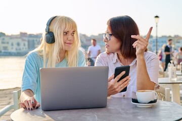 Serious mother and teenage daughter together in outdoor cafe looking at laptop