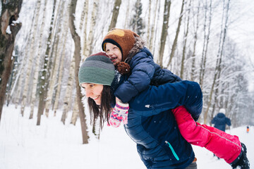Fototapeta na wymiar Young mother and child girl on a winter walk in nature playing with snow. A girl on a sled with gifts on the eve of the new year in the park. Two sisters walk in a New Year's park
