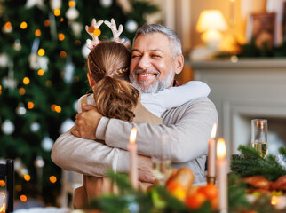 Little girl granddaughter embracing happy smiling grandfather during Christmas dinner at home