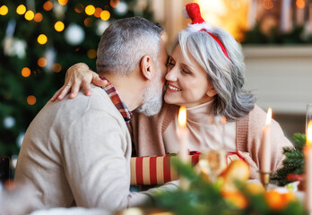 Happy senior family couple hugging and exchanging Christmas presents during festive dinner at home