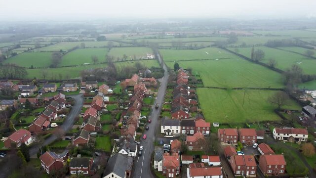 A van / lory driving through a small town in the UK on a misty day. 4K drone footage following a van / lorry. English countryside, in winter. Small town from above. Great Broughton. 