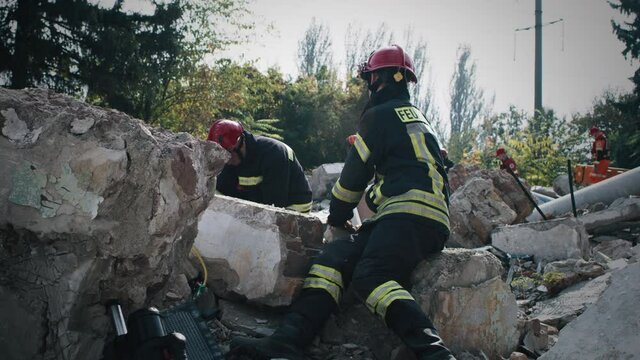 Men in protective uniform and hardhats sitting on concrete rubble and searching for survivors after earthquake
