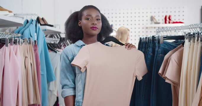 Portrait of young beautiful african american woman standing in clothing store and showing off in front of camera in new outfit with shopping packages.