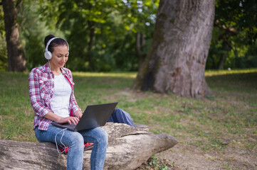 Fototapeta premium Young woman freelance entrepreneur working on her laptop computer out in the nature. Global wi-i network. Using mobile information devices outdoors
