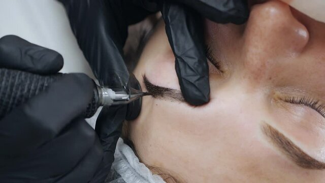 A special needle tattoo machine makes permanent makeup correction of a young woman