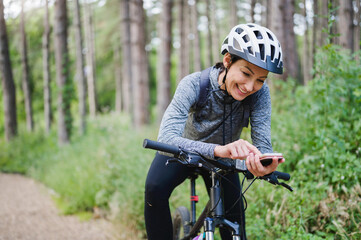 Young female cyclist using a mobile smartphone outdoors in the nature