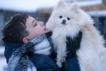 A young man in a winter scarf, cuddling and hugging his dog, a close friendly love affair between a boy and a pet