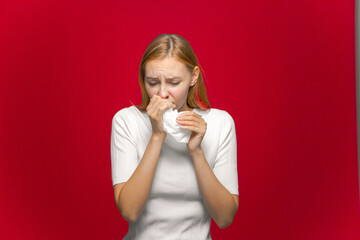 Sick girl suffer chill, flu. influenza symptom or allergy covering runny nose with handkerchief on red studio background