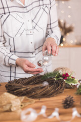 Woman artisan making Christmas holiday wreath on a table among by New Year's decor