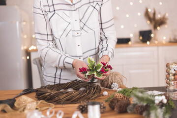 Woman artisan making Christmas holiday wreath on a table among by New Year's decor