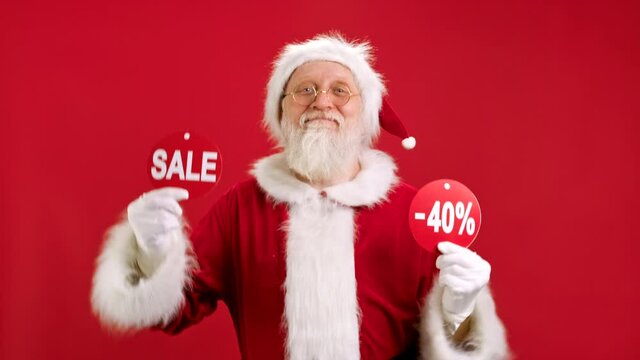 Christmas SALE -40 Off. Cheerful Santa Claus is Dancing and Joyful From Christmas Sale Holding Two Banners With Inscription SALE and -40 Off Showing Off Inscriptions to Camera on Red Background.