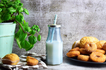 In the kitchen, glass bottle with milk and a straw. Outline of home, with sweets, stone background, entrance of light on the side.