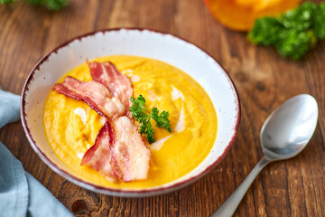 Fresh pumpkin soup with cream and bacon, garnished with a sprig of parsley. Autumn food. Seasonal soup