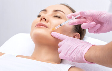 Cosmetologist makes rejuvenating anti wrinkle injections on the face of a beautiful woman. Female...