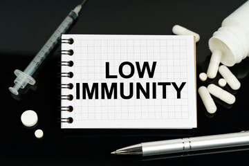 On the black surface are pills, a syringe and a notebook with the inscription - low immunity