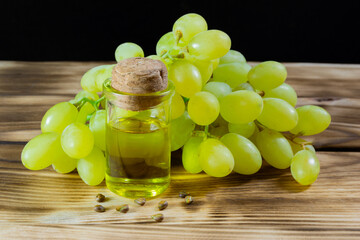 Grape oil seed in small vintage bottle. Heap of grape seeds with green slices and cold press organic essential oil, tincture, extract, infusion on wooden rustic background closeup
