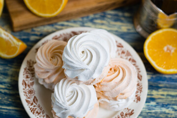 Delicious marshmallow with orange filling in a vintage plate, sliced orange on a cutting board and tea in a glass.