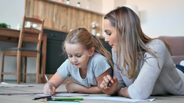 Happy young mother and cute daughter drawing picture together use multicolored pencil paper sheet