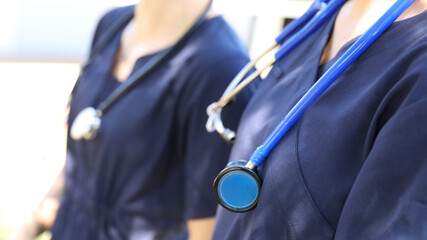Two female medical practicioners in blue uniform with stethoscopes around their necks. Nursing or...