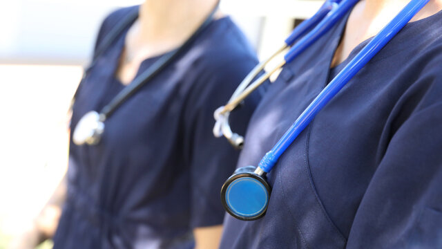 Two female medical practicioners in blue uniform with stethoscopes around their necks. Nursing or doctors in hospital gowns or clothes. Health, hospitals and medical themed image.