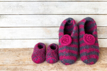 Self knitted felt slippers for mother and her kid against wooden board in the background - with...