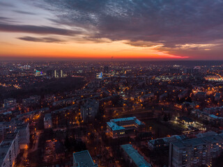 Fototapeta na wymiar Aerial sunset orange vibrant view on Kharkiv city, Pavlove pole. Night lights on streets of residential district and scenic cloudy sky after sunset. Moody illuminated streets rooftop