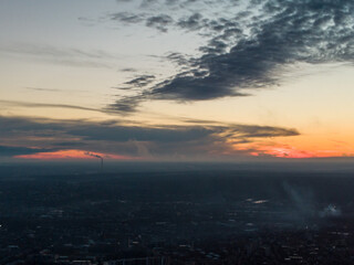 Aerial dark moody cloudy sunset evening view on residential city district. Industrial pipe with smog, gray buildings and red sun on horizon