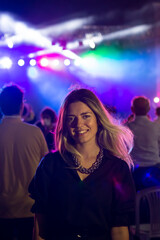 A girl laughing in concert area. There is purple light in there. Everyone taking photos. Crowded.