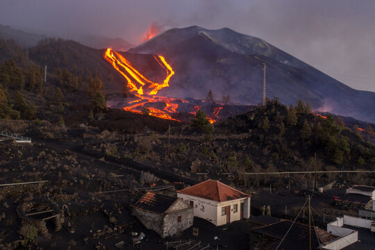 Aerial view of a house with Volcan Cumbre Vieja in background, a volcano during eruption near El Paraiso town, Las Manchas, La Palma Island, Canary Islands, Spain.
