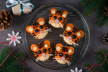 Tartlets in the form of funny tiger cubs for the New Year 2022 from sausage, cheese, carrots and black olives on a brown background