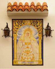 Die allerheiligste Maria in Trauer gemalt auf Kacheln, die eine Außenwand einer Kirche in Algeciras schmückt. Von oben geschützt durch einen Baldachin und links und rechts beleuchtet durch 2 Laternen