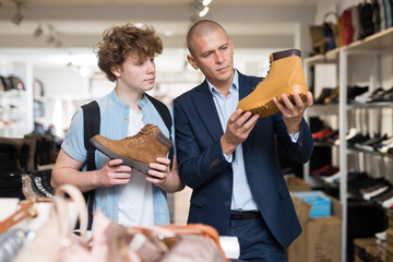 Portrait of man and teenage boy shopping for mens shoes in store, choosing demi-season lace up boots.