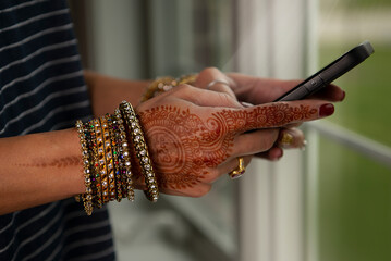 Woman's hands with henna typing on phone 