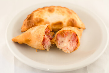 empanada rellena de jamon y queso cortada a la mitad en plato blanco