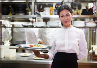 Portrait of smiling asian waitress with ordered dishes in kitchen of modern restaurant