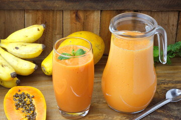 Homemade papaya smoothie with mint in cup and glass jar on rustic wooden table