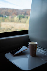 Kawa oraz telefon na rozkładanym stoliku przy fotelu pasażera, w wagonie pociągu pendolino pkp intercity. Za oknem ładny widok pełen roślinności © Katarzyna